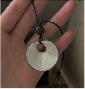 Detail of a round pendant with brushed metal texture and a brown wooden bead on a black cord