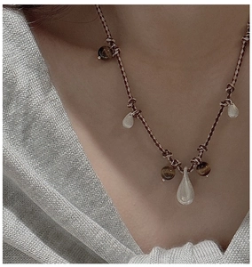 Detail of nomad style woven cord necklace with tiger eye beads and teardrop silver pendant