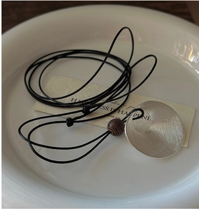 Detail of brushed silver pendant with a natural wood bead on a black cord necklace