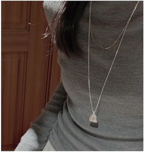 Détail du collier pendentif sac en argent S925 superposé sur un pull en maille grise
