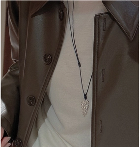 Close-up of S925 silver grape pendant on black cord worn over a brown leather jacket
