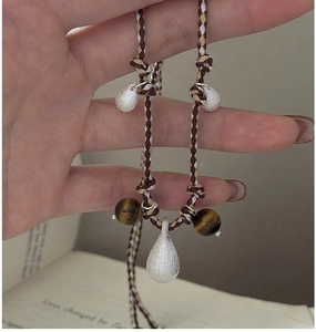 Macro shot of silver teardrop charms and tiger eye beads on a woven cord necklace