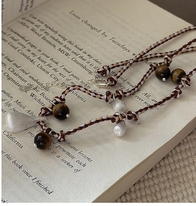 Detailed view of woven S925 silver necklace with tiger eye beads on an open book