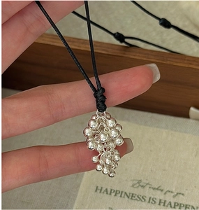 Detail of silver grape cluster pendant necklace on a black rope cord shown on hand