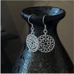Detail of silver drop earrings with intricate hollow floral lace pattern on a ceramic pot