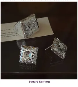 Macro shot of silver square geometric earrings with diamond-cut texture on dark surface