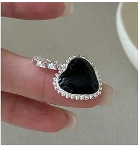 Detail of a vintage S925 silver heart pendant with black enamel held in hand for scale