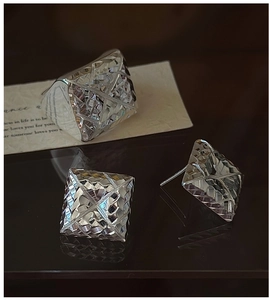 Close-up of geometric square cut silver ring and stud earrings with reflective metal finish