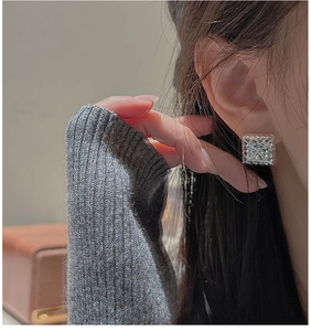 Close-up of a square silver stud earring with textured surface worn by a model