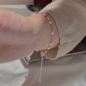 Main portant un bracelet minimalist en argent S925, cordon rouge et perles blanches