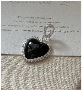 Macro detail of S925 silver heart charm with black enamel and beaded edge on fabric