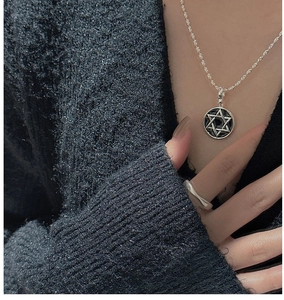 Macro detail of S925 sterling silver hexagram pendant and wavy ring on knitted fabric