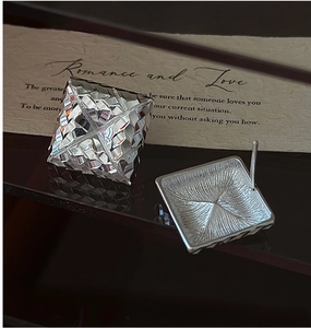 Macro detail of square silver earrings with diamond-cut grid texture and pin back