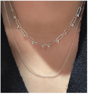 Close-up of golden double-layer necklace with paperclip and beaded chain on neck
