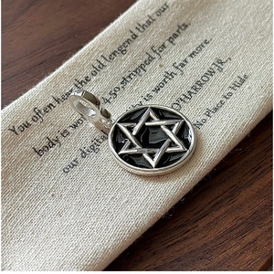 Close-up of S925 silver hexagram pendant with black enamel finish on vintage beige fabric