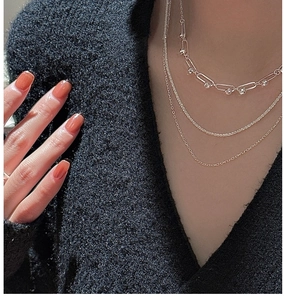 Detailed view of layered silver-tone necklaces with paperclip links on a black knit sweater