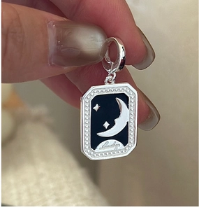 Macro shot of silver rectangular charm with black enamel star moon and Lucky engraving