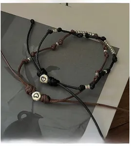 Detail von handgewebten Kordelarmbändern mit Herzperlen auf rustikalem Holztisch