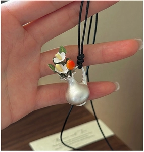 Vue macro du pendentif vase en argent S925 avec fleurs et baie rouge sur un cordon noir