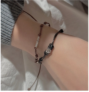 Detail von geflochtenen Armbändern mit Herzanhänger und Silberringen am Handgelenk