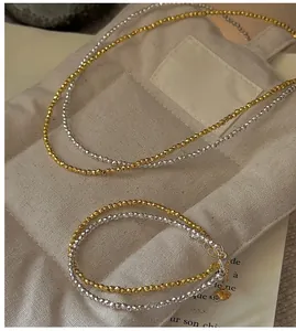 Détail d'un collier de perles facettées bicolores avec petit pendentif cœur sur lin