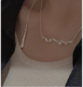 Close-up of S925 silver wave necklace with white pearls on a model wearing a sweater