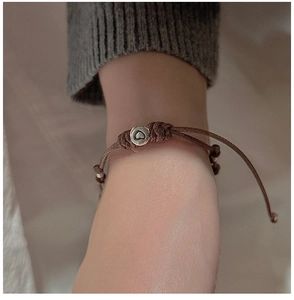 Nahaufnahme eines handgewebten braunen Armbands mit silberner Herzperle am Handgelenk