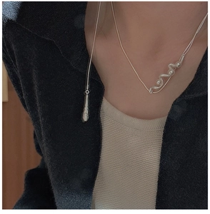 Detail of S925 sterling silver wave necklace with pearls on a model wearing a cardigan