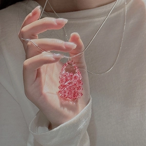 Pink beaded mini bag pendant necklace with silver chain on beige knitted sweater