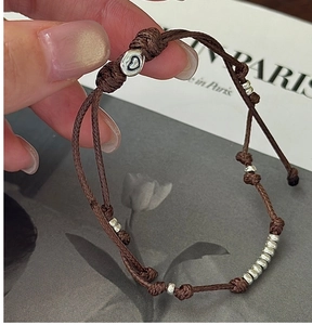 Detailansicht eines braunen Wachskordel-Armbands mit Silberperlen und Herzanhänger