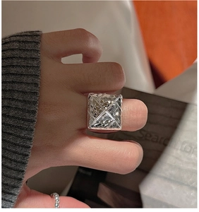 Macro shot of silver ring with diamond-cut texture on large square surface for women