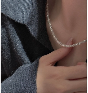 Detailed view of a shiny S925 sterling silver woven chain necklace worn on a dark knit top