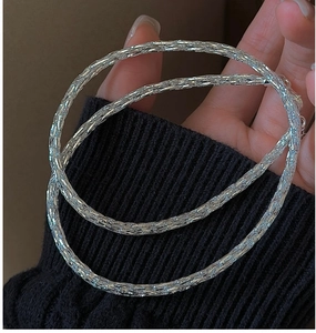 Detail shot of shimmering silver bangles with textured finish worn over a black sleeve