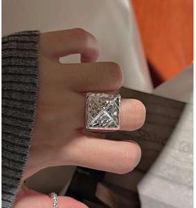 Macro view of square silver ring with geometric diamond-cut patterns on finger