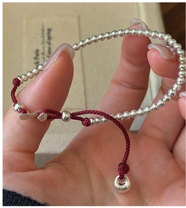 Detail of red cord bracelet with silver beads and adjustable bear-shaped clasp design