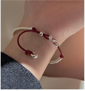 Close-up of red woven bracelet with S925 silver charms and beads on a woman's wrist