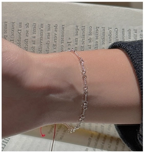 Detail of a minimalist S925 silver braided chain bracelet worn on a wrist over a book