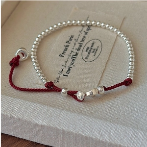 Detailed shot of handmade red cord bracelet with polished S925 silver beads and flower charm