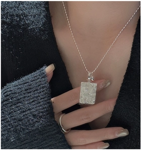 Detail of vintage silver daisy pendant necklace with embossed flower on black knit background