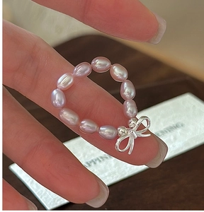Macro shot of freshwater pearl ring with a silver bow pendant on a woman's finger