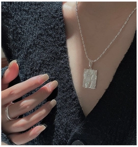 Detailed shot of silver daisy pendant and minimalist band ring on black knitwear
