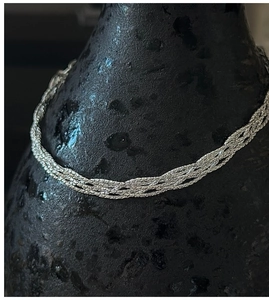 Macro detail of braided S925 sterling silver chain texture against a dark ceramic vase