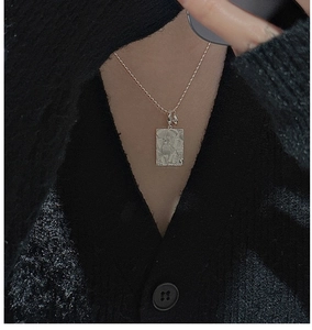 Detailed close-up of a silver rectangular daisy pendant with floral relief on a bead chain