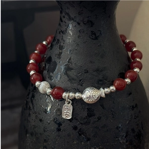 Détail du bracelet en agate rouge avec charme de poisson en argent et plaque Ping An