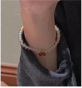 Close-up of beaded cherry bracelet with red cherry charms and yellow flower on a wrist
