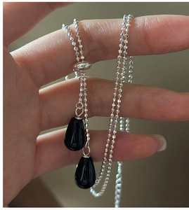 Détail du collier à billes argentées avec pendentifs gouttes en agate noire et curseur