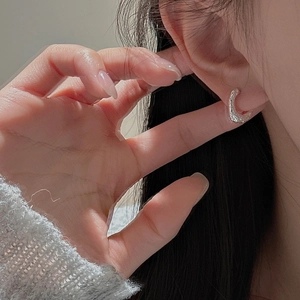 Boucles d'oreilles créoles C en argent S925 avec texture martelée portées par un modèle