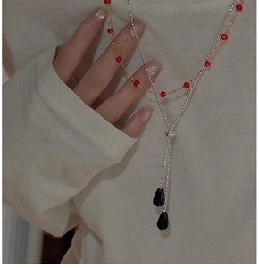 Détail d'un collier double rang avec perles rouges et pendentifs goutte noirs portés