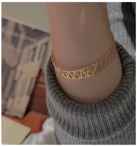 Detail eines gewebten goldenen Gliederarmbands am Handgelenk mit Strickpullover