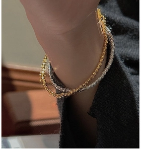 Close-up of stacked gold and silver faceted bead bracelets on a wrist with a cozy knit sleeve